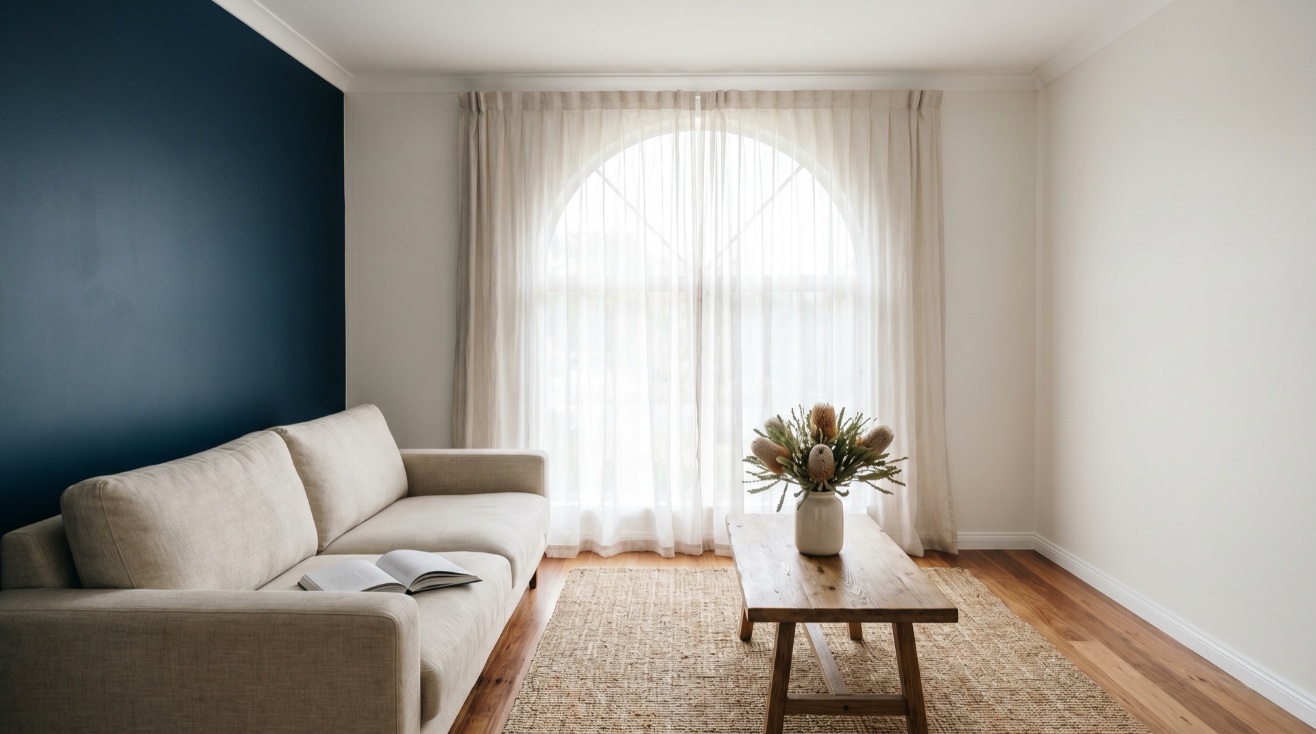 Coastal living room with deep navy feature wall, linen sofa and arched window